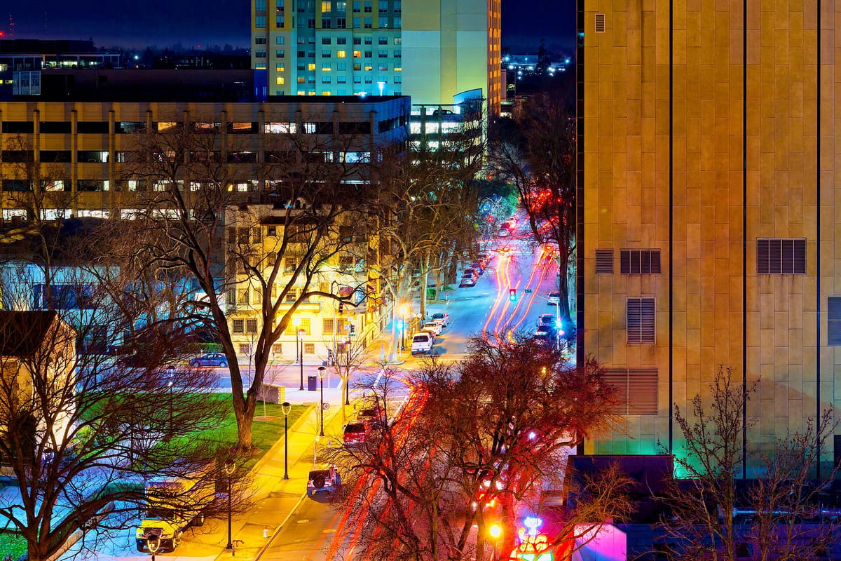 A Midtown street at night, lit by traffic and shop signs